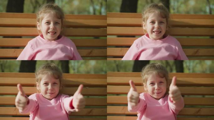 微笑的小女孩在春季公园的长凳上竖起大拇指