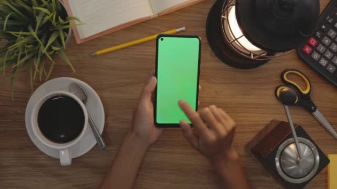 俯视图女人在智能手机的绿色屏幕上使用手指滑动。爱好表背景。色度键。绿屏手机。