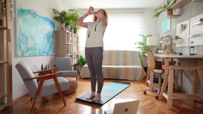 灵活的白人妇女在笔记本电脑上进行在线瑜伽课，同时在家锻炼