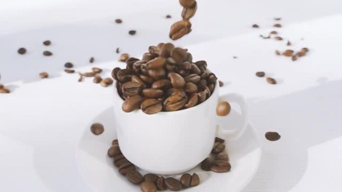咖啡豆落入木制白色桌子上的白色杯子中。满溢咖啡豆的杯子。具有速度斜坡效果的4k原始视频。在高速电影摄