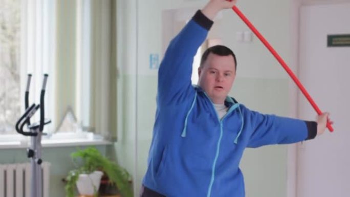 一名患有唐氏综合症的男子用体操棒参加运动，并向健身房的两侧弯曲。