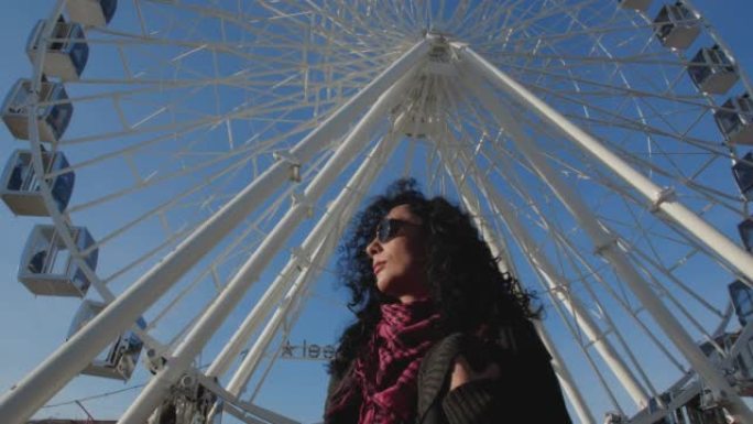迷人的时尚黑发女孩，一个戴着高德太阳镜的卷曲非洲头发的女人，在阳光明媚的日子站在城市广场上。在白色摩