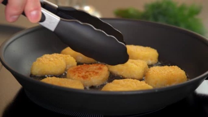 厨房钳子在热煎锅中用铁热油翻转炸鸡块。用脆皮炸块。