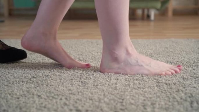 一个女人的特写镜头脱下鞋子，赤脚躺在地毯上
