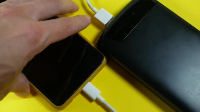 带usb的黑色电源正在为黄色背景的智能手机充电。