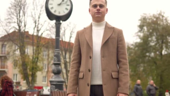 街道时钟背景下，一个穿着棕色外套的英俊时髦男人的肖像。新时尚服装系列