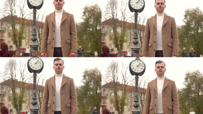 街道时钟背景下，一个穿着棕色外套的英俊时髦男人的肖像。新时尚服装系列