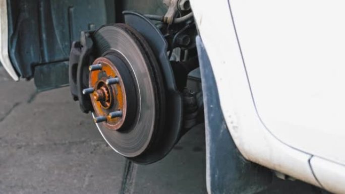 汽车轮毂，在车库车间轮胎更换过程中暴露出制动盘和制动片，凸耳螺母铺在地面上