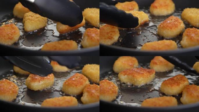 厨房钳子在热煎锅中用铁热油翻转炸鸡块。小吃、快餐