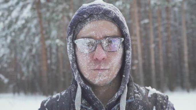冬日森林里一个戴着眼镜的冻僵男子，在一场暴风雪过后，满身是雪，面带微笑地看着镜头…
