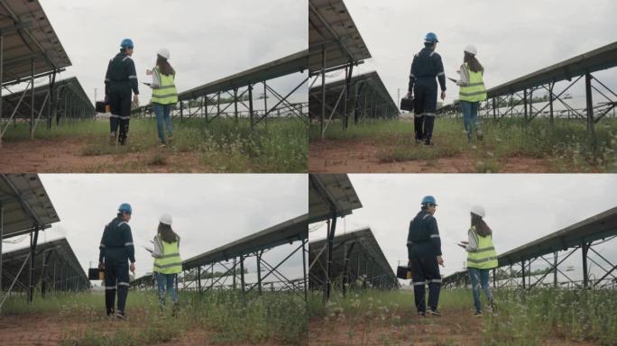 两名穿着制服和安全帽的工人在太阳能农场的太阳能站检查电源