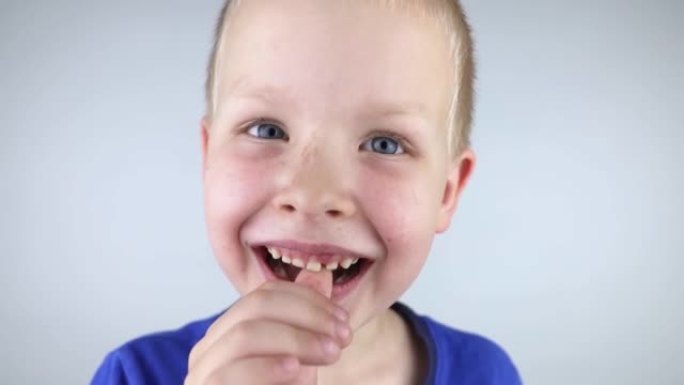 松动的乳牙。金发男孩用手触摸一颗乳牙，展示他是如何移动的。成长的阶段。