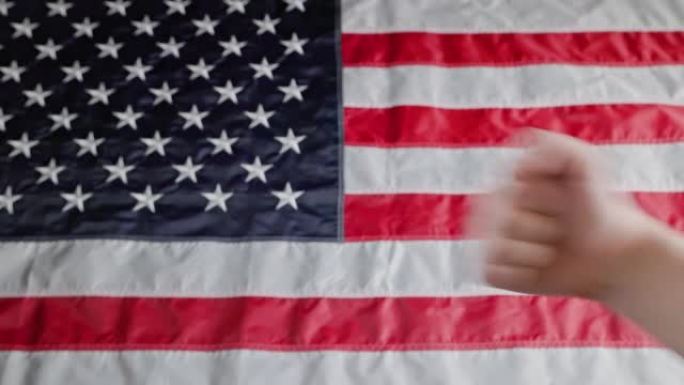 白人的手在模糊的美国国旗前做出了大拇指朝上和大拇指朝下的手势