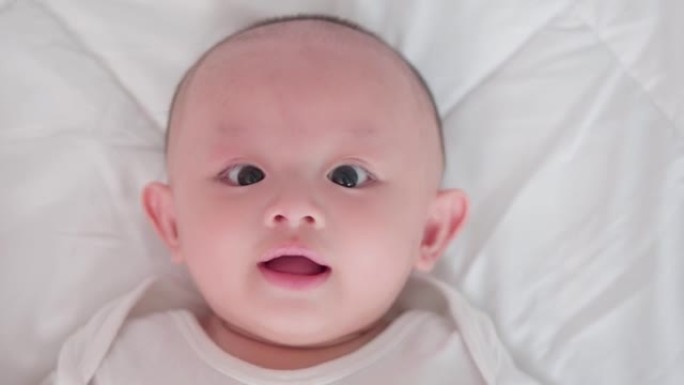 脸部特写肖像可爱的亚洲新生婴儿躺在白色床上玩耍看着相机笑着笑脸。天真的小新婴儿可爱。父母身份和母亲节