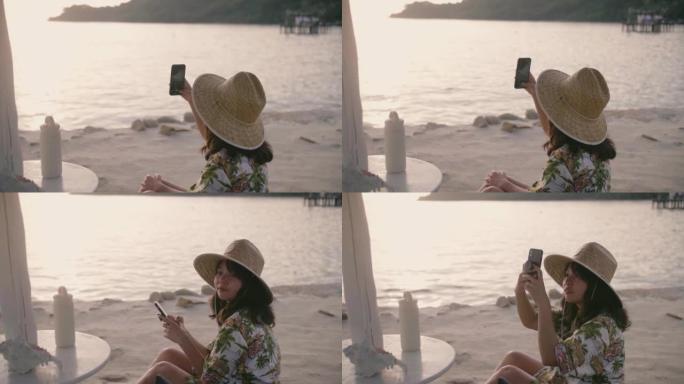 日落时分，女人在海滩用手机在度假村前拍照。