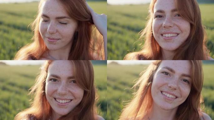 微笑的姜女人的肖像在户外的绿色麦田里拉直头发。性感的女孩，留着长长的红头发，在镜头前看着雀斑。特写年