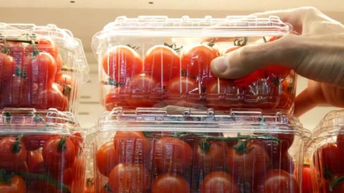 在冰箱架子上的塑料包装盒中，许多樱桃番茄的特写镜头，一只雄性手拿了一个