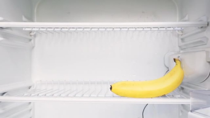 这个人的手打开一个空冰箱，拿走一根香蕉。概念性4k原始视频。经济危机、粮食短缺、贫困的想法。