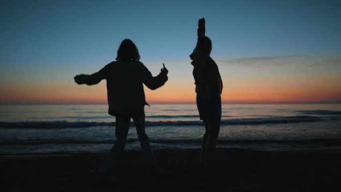 晚上，两个女孩在海边日落时跳舞。