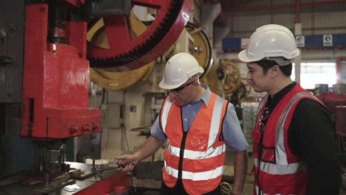 高级工程师戴上带磁性的安全镜和头盔，并培训年轻工程师在工厂操作液压机。