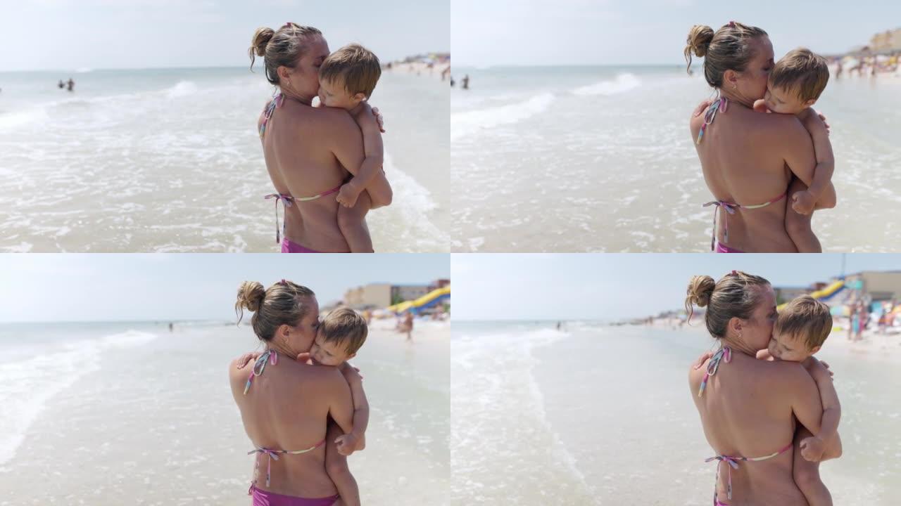 穿着夏季比基尼的妈妈抱着一个想在度假时在海边的海滩上睡觉的婴儿
