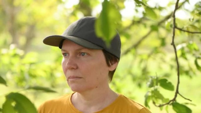 在核桃果树果园中摆姿势的戴着卡车司机帽子的女农民肖像