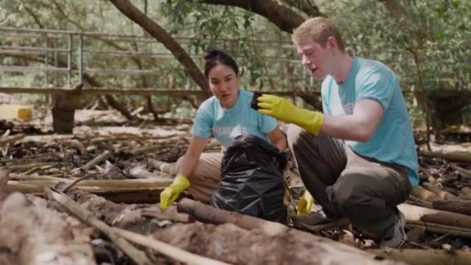 高加索年轻成年男子和亚洲年轻成年妇女志愿者戴着黄色橡胶手套，一起帮助将垃圾，塑料袋和塑料瓶收集到垃圾