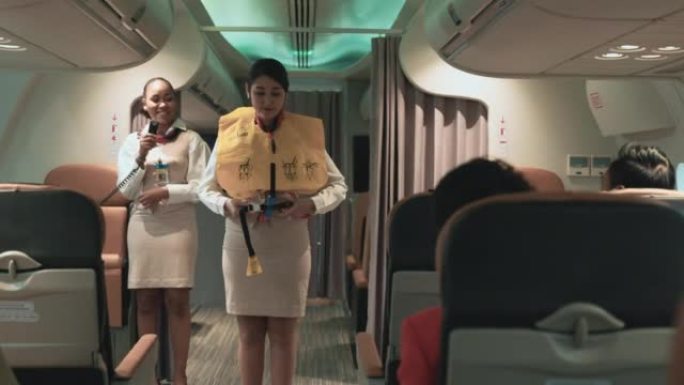 两名身穿制服的女乘务员解释并演示了如何在起飞前在机舱中使用救生衣以保护事故。