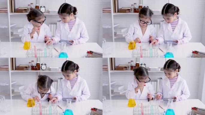 4K，两个亚洲女孩，站在科学教室，混合颜料，做化学实验，用挤压管挤出彩色水滴到测试杯，另一个人拿着笔