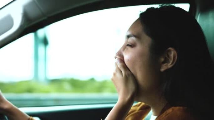 后视镜。年轻的亚洲女司机昏昏欲睡。她打了个哈欠，正要睡着。打瞌睡，长时间开车，睡眠不足