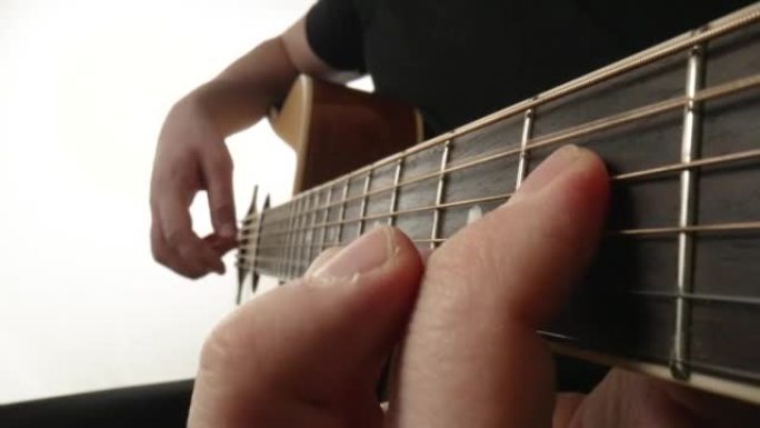 音乐家在白色背景上演奏原声吉他。男人的手指触摸吉他的琴弦，使它们振动并演奏歌曲的旋律。木制指板吉他和
