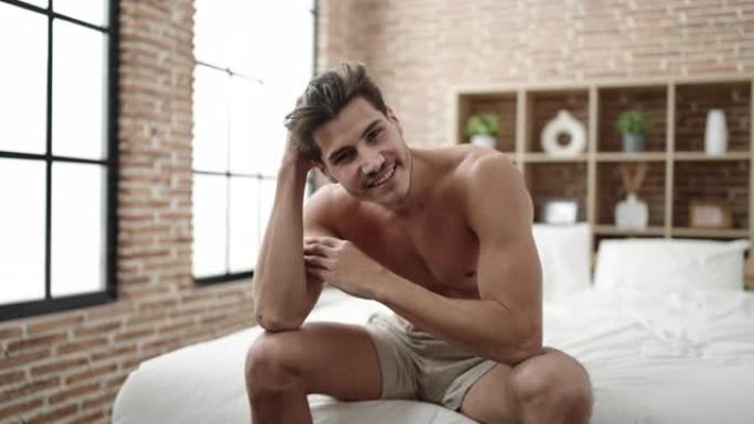 年轻的西班牙男子微笑着自信地坐在卧室的床上