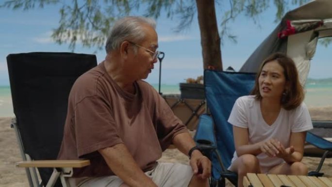 老人在海滩上旅行的肖像，积极的祖父与家人一起度假，快乐的叔叔坐在露营的桌椅上在海上放松