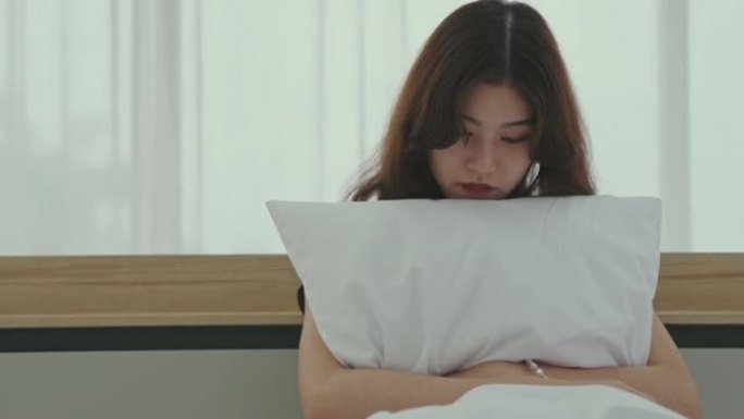 悲伤的女人坐在家里的床上拥抱枕头的肖像