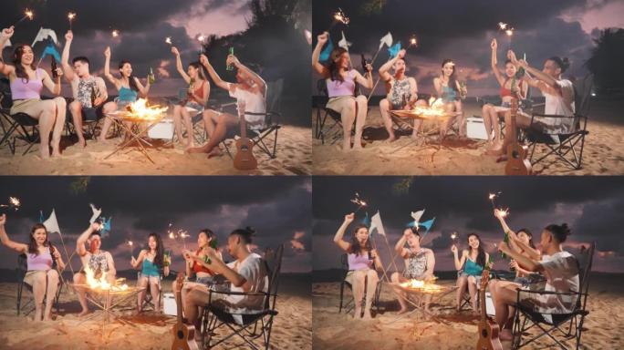 一群亚洲年轻男女晚上在海滩上聚会。迷人的朋友旅行者在海边露营时唱歌跳舞，一起享受热带海岛的假期旅行