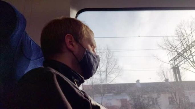 一个戴着黑色面具的男人坐在火车上，看着窗外。旅行时预防感染和疾病。为文本复制空间