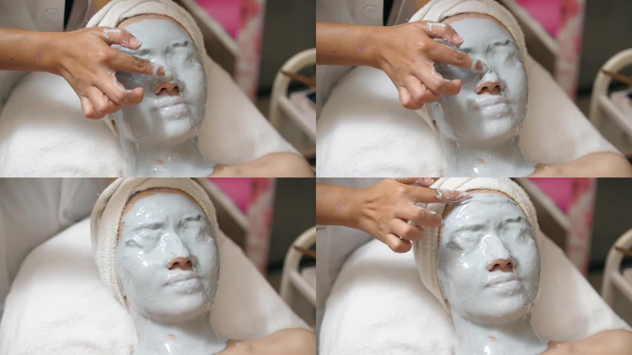 年轻的亚洲妇女在水疗中心使用维生素面膜和面部按摩