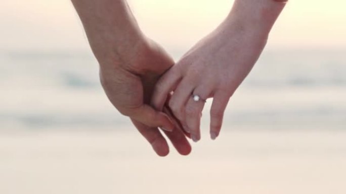 一对面目全非的夫妇牵着手，戴着订婚戒指。一个男人和女人在海滩上求婚后的特写镜头