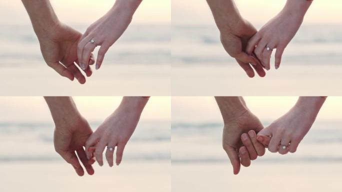 一对面目全非的夫妇牵着手，戴着订婚戒指。一个男人和女人在海滩上求婚后的特写镜头