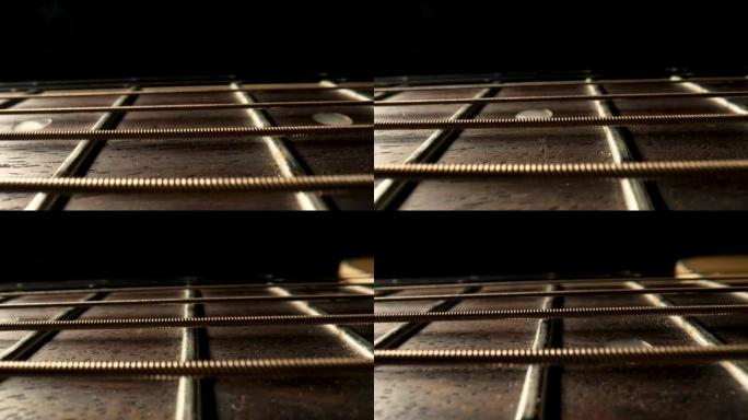 黑色背景上带有金属琴弦和琴弦的原声吉他琴颈的滑动微距拍摄。吉他极限特写的棕色木制指板。创作音乐的弦乐