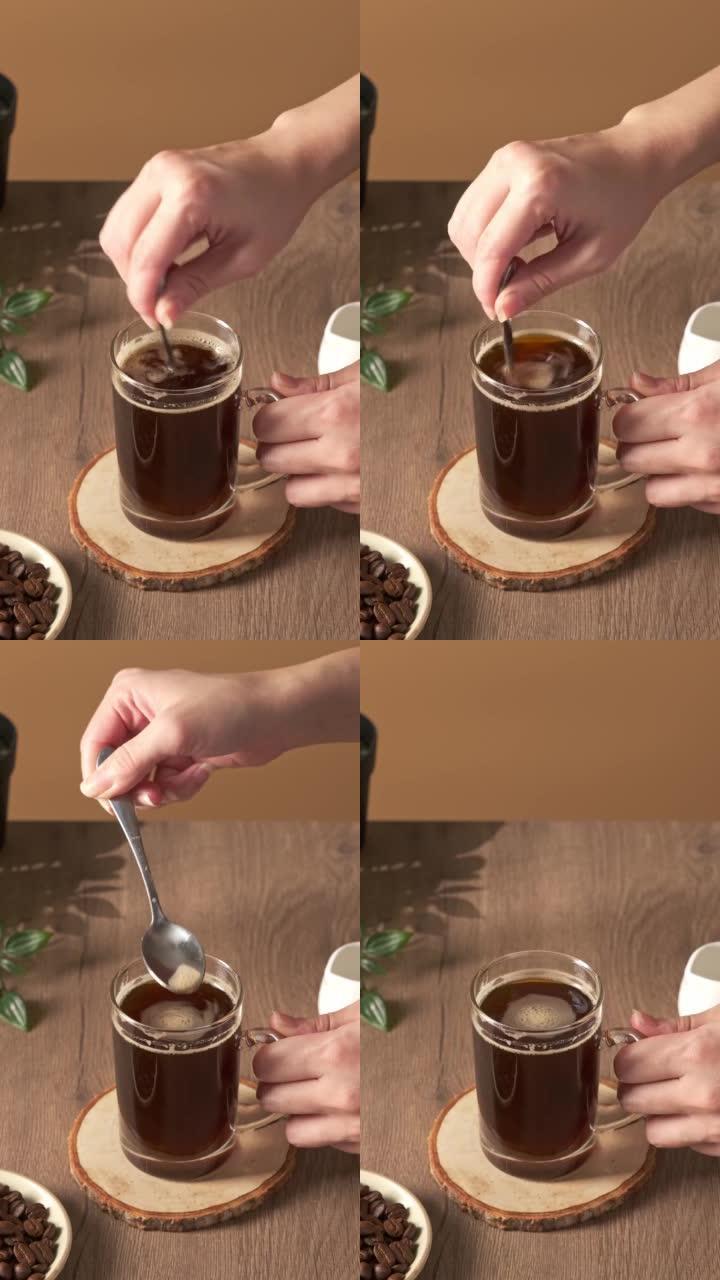 垂直，4k视频，女性用勺子搅拌咖啡。一杯浓缩咖啡热饮健康，放在咖啡馆或家里的木质桌子上，自然清淡。早