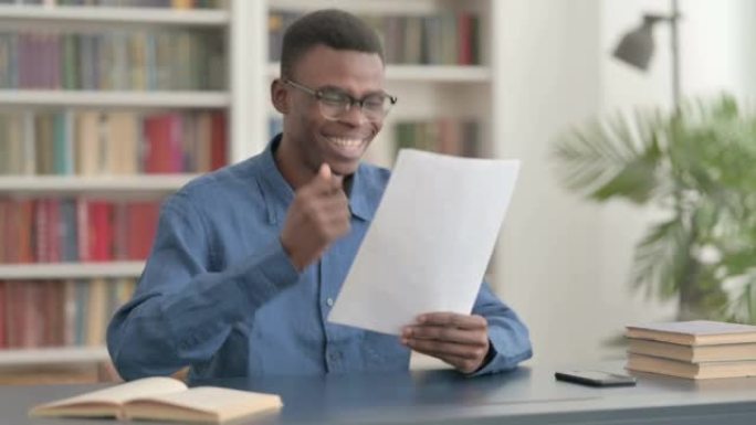 年轻的非洲男子在办公室阅读文件时庆祝成功