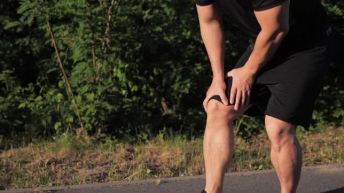 运动型亚洲运动员跑步，日落时突然感到腿部疼痛痉挛。男子在户外慢跑时停止按摩膝盖伸展，外伤。扭伤剧烈疼