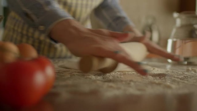 站在厨房里的女性手滚动面团的特写。女厨师在围裙烹饪自制比萨饼。手持摄像机。