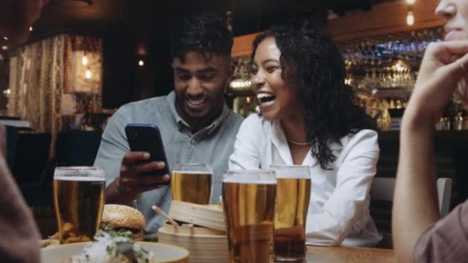 一家餐馆的两个多种族朋友看着他们用一部手机拍的自拍照。
