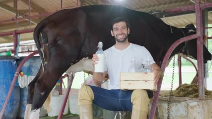 高加索男性奶农的肖像在牛棚里拿着一瓶牛奶。年轻英俊的男性农业农民微笑着看着相机在畜牧业用幸福挤奶后