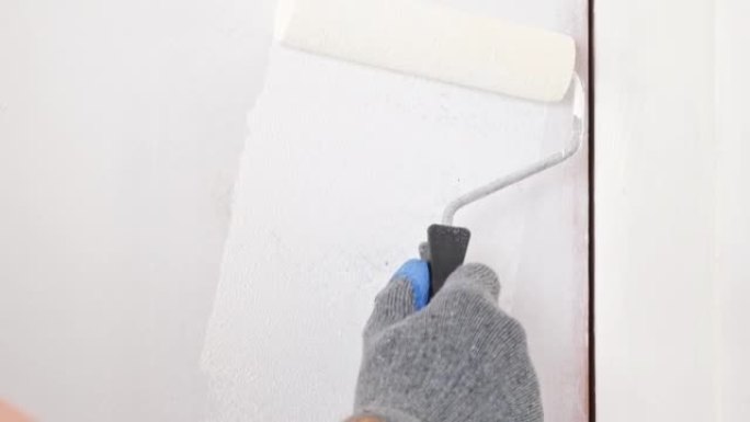 一个男人把木门涂成白色。画家用泡沫涂料滚筒涂白色丙烯酸涂料