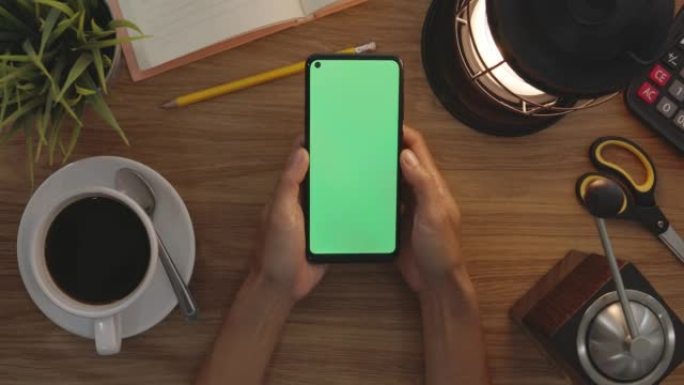 俯视图女人在智能手机的绿色屏幕上使用拇指触摸。爱好表背景。色度键。绿屏手机。