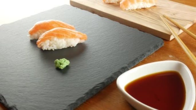 三文鱼泥鱼寿司、酱油和芥末酱放在石板上，桌子上有木砧板，用筷子