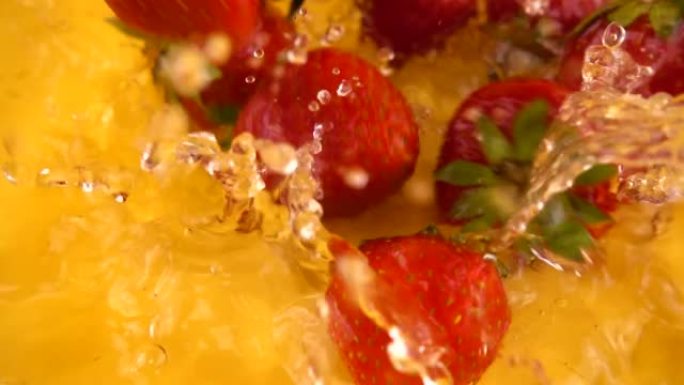在橙色背景下将草莓掉入水中。慢动作。
